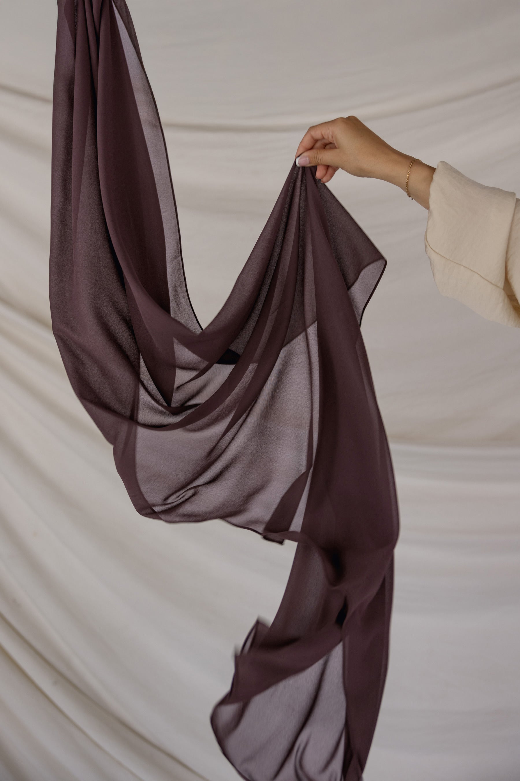 Brown chiffon hijab being held against a neutral background