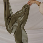 Green chiffon hijab being held against a neutral background