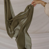 Green chiffon hijab being held against a neutral background