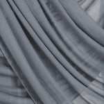 Close-up of draping folds of the dark sage hijab over a neutral backdrop.