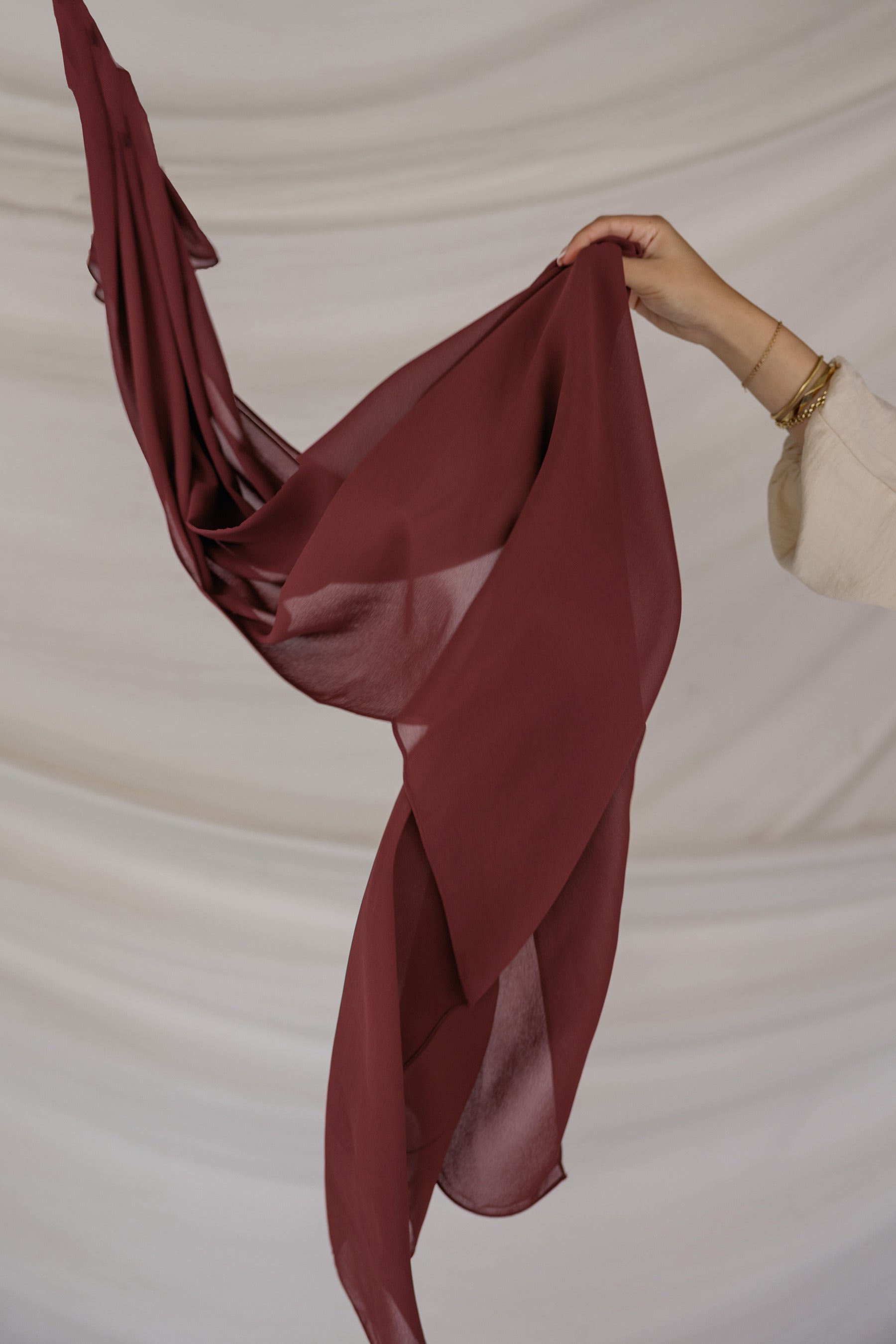 Red chiffon hijab being held against a beige background