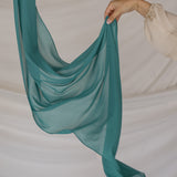 Teal chiffon hijab being held up against a neutral background