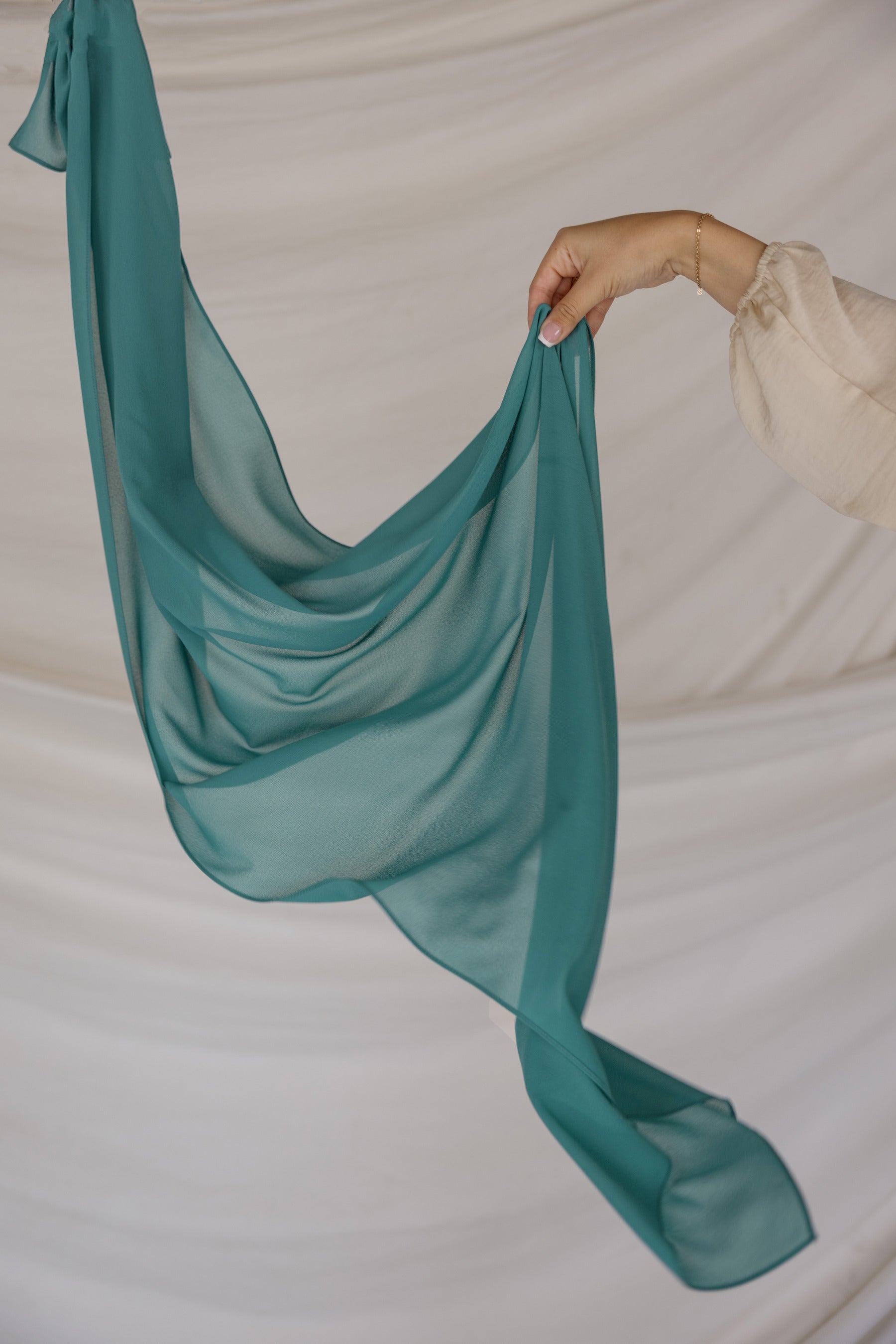 Teal chiffon hijab being held up against a neutral background
