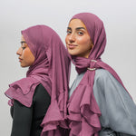 Two women modeling ruffled hijabs in a dusty mauve shade, shown from the side and back against a plain light gray studio background.