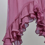 A close-up of a dusty pink ruffled fabric, likely a dress or skirt, showing the layered, semi-sheer texture against a neutral gray background.