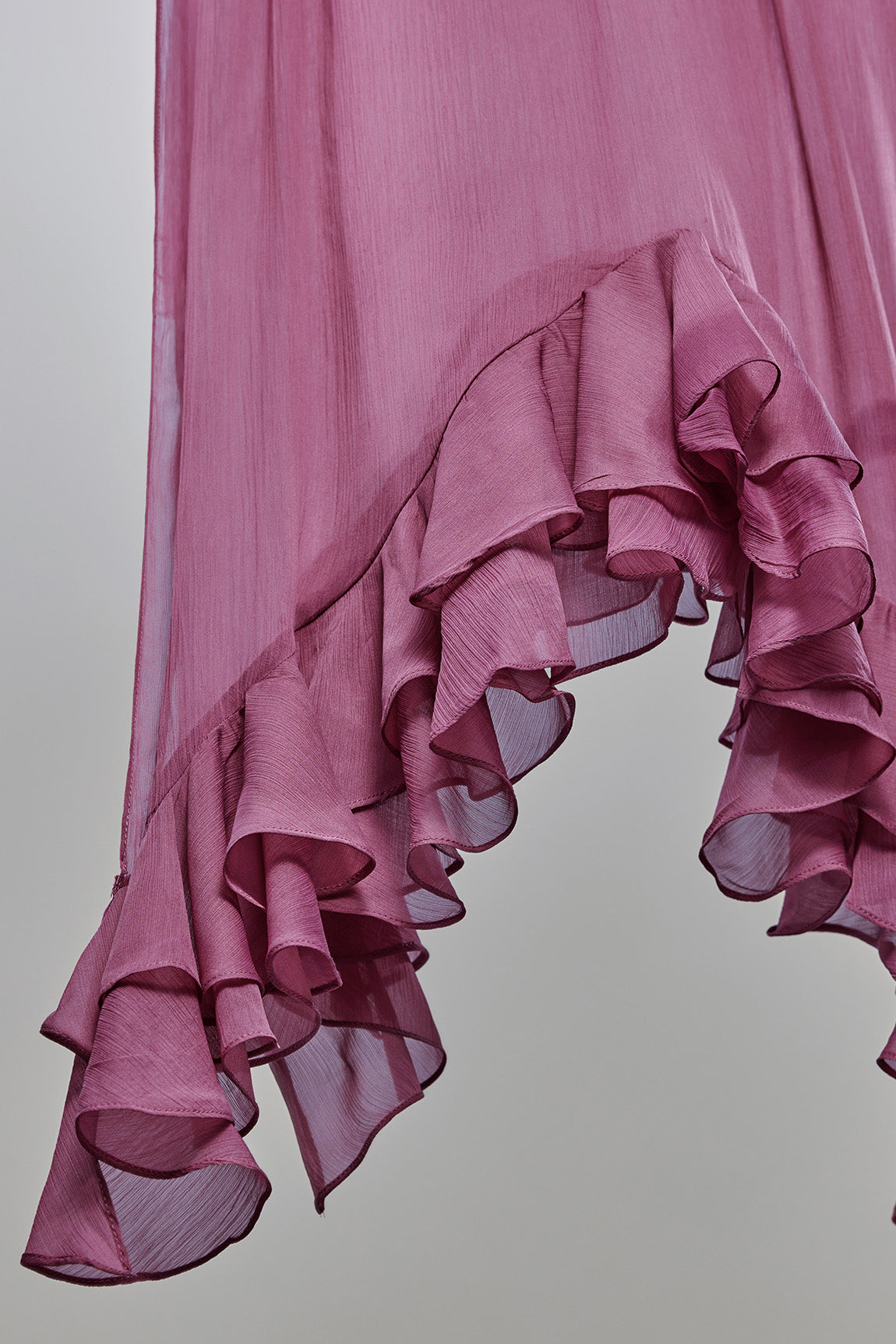 A close-up of a dusty pink ruffled fabric, likely a dress or skirt, showing the layered, semi-sheer texture against a neutral gray background.