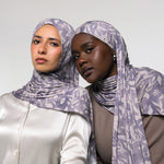 Two women wearing matching patterned hijabs in a studio setting against a light gray background.