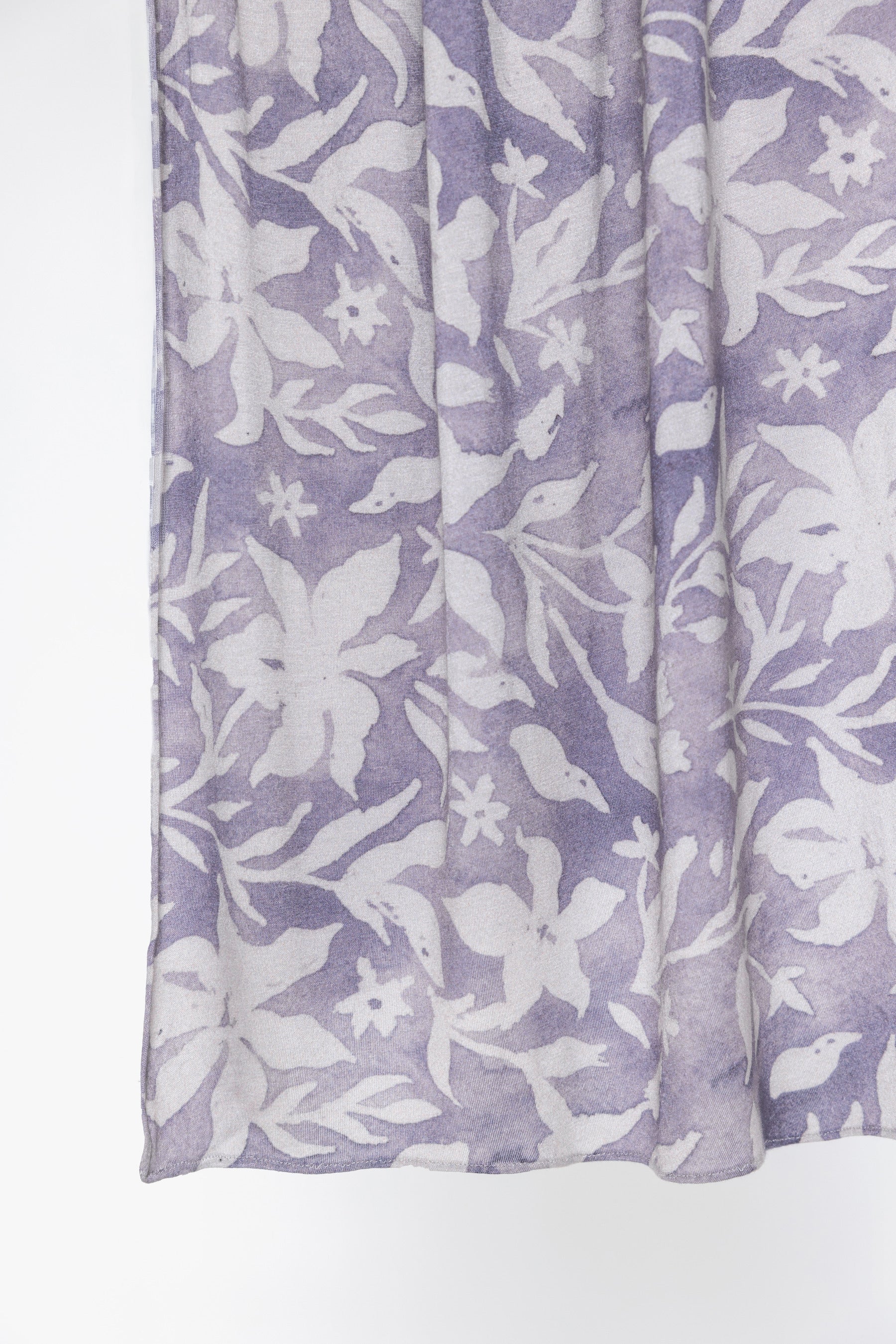 A close-up of a lavender and white floral patterned fabric, likely a scarf or lightweight wrap, shown hanging against a plain white background.