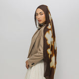 Woman wearing a brown and white patterned hijab on a plain background