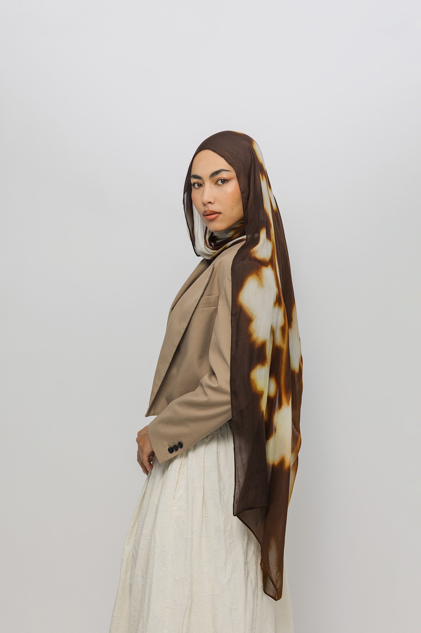 Woman wearing a brown and white patterned hijab on a plain background