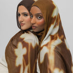 Two women wearing brown patterned hijabs against a white background