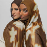 Two women wearing brown patterned hijabs against a white background