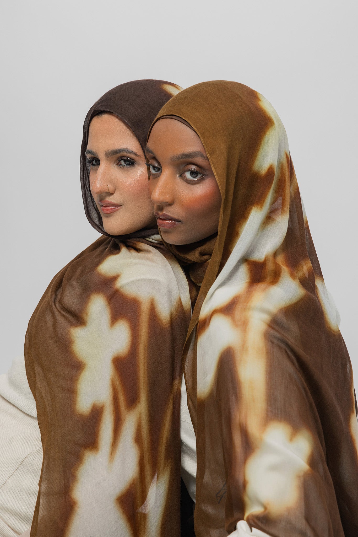 Two women wearing brown patterned hijabs against a white background