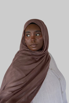 Model wearing taupe colored hijab against backdrop.