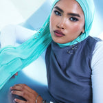 woman wearing mint green hijab and blue vest with white long sleeve shirt.