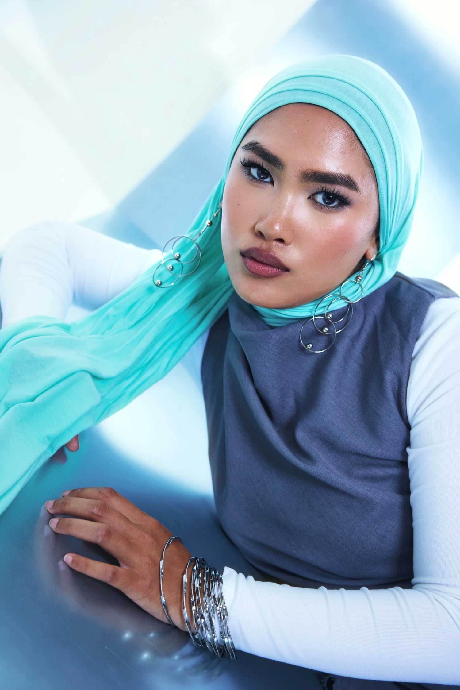 woman wearing mint green hijab and blue vest with white long sleeve shirt.