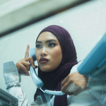 A woman wearing a deep plum purple hijab and a white blouse is shown in a stylized, grainy photograph, holding a light blue landline telephone receiver to her ear.