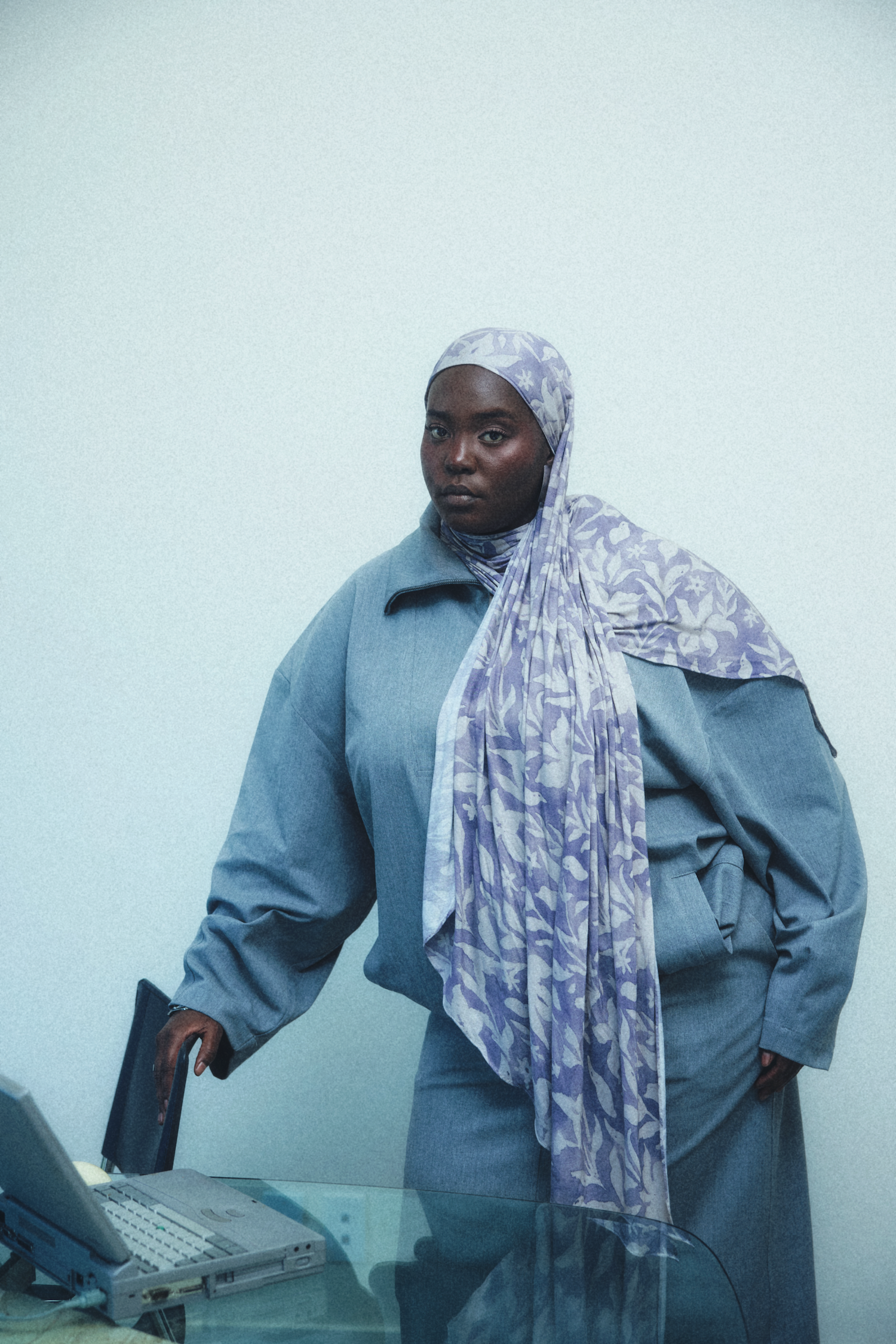 A woman wearing a light purple and white patterned hijab in a soft blue track suit. 