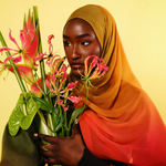 Woman holding a bouquet of flowers against a yellow background wearing a mango ombre hijab