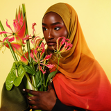 Woman holding a bouquet of flowers against a yellow background wearing a mango ombre hijab