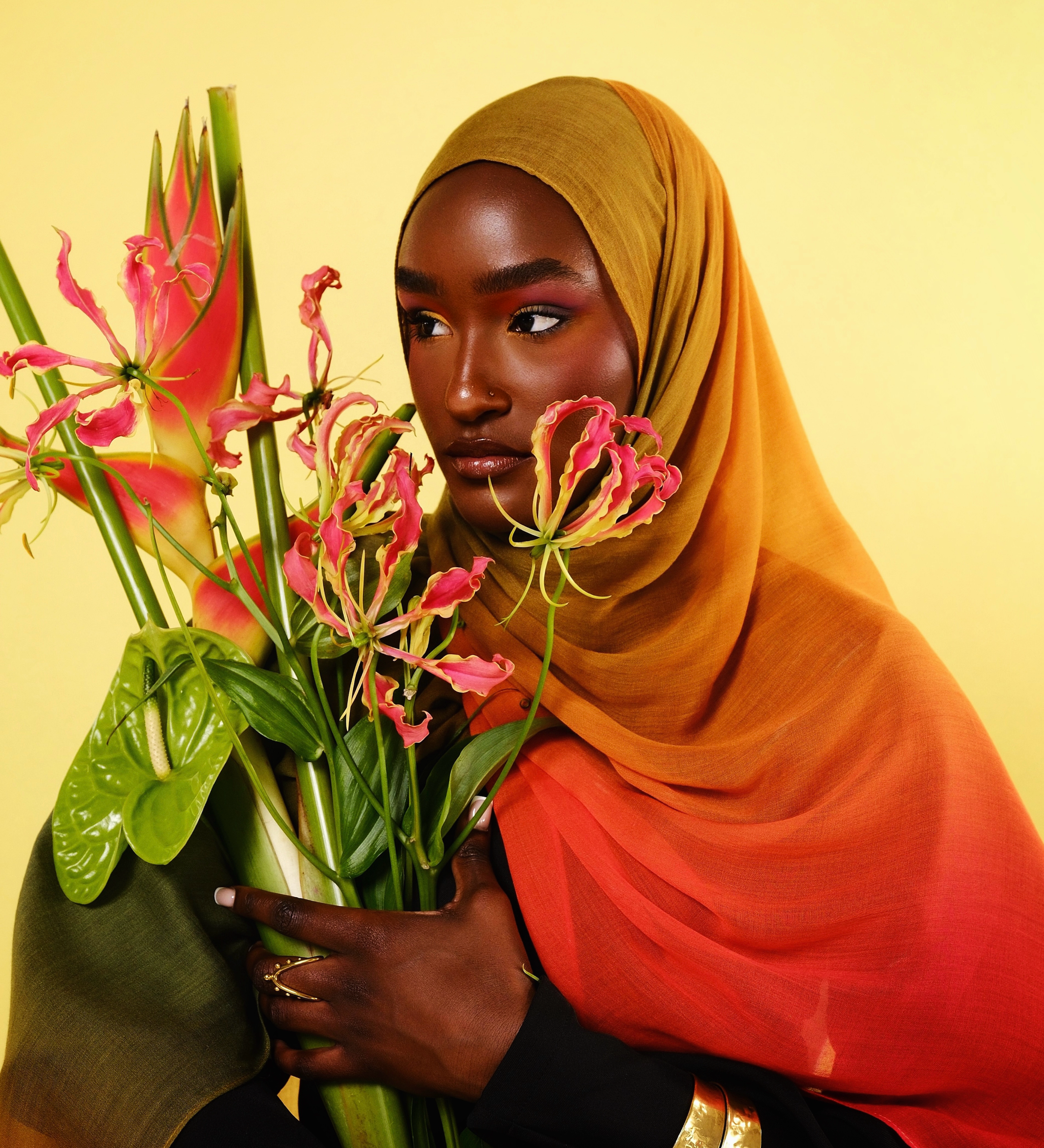 Woman holding a bouquet of flowers against a yellow background wearing a mango ombre hijab