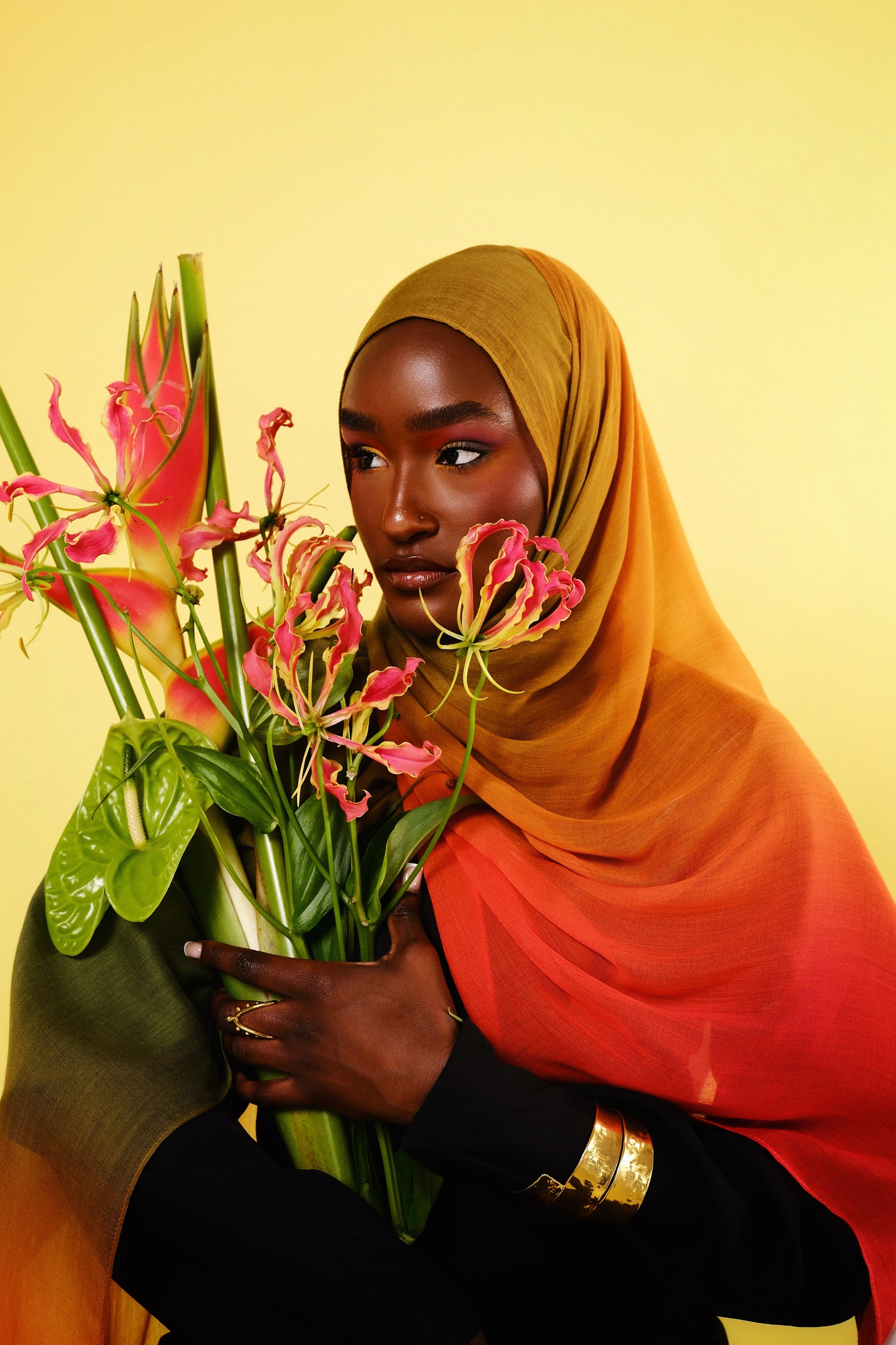 Woman holding a bouquet of flowers against a yellow background wearing a mango ombre hijab