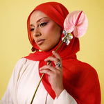 Woman wearing a red hijab holding a pink flower against a yellow background