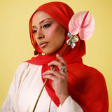Woman wearing a red hijab holding a pink flower against a yellow background