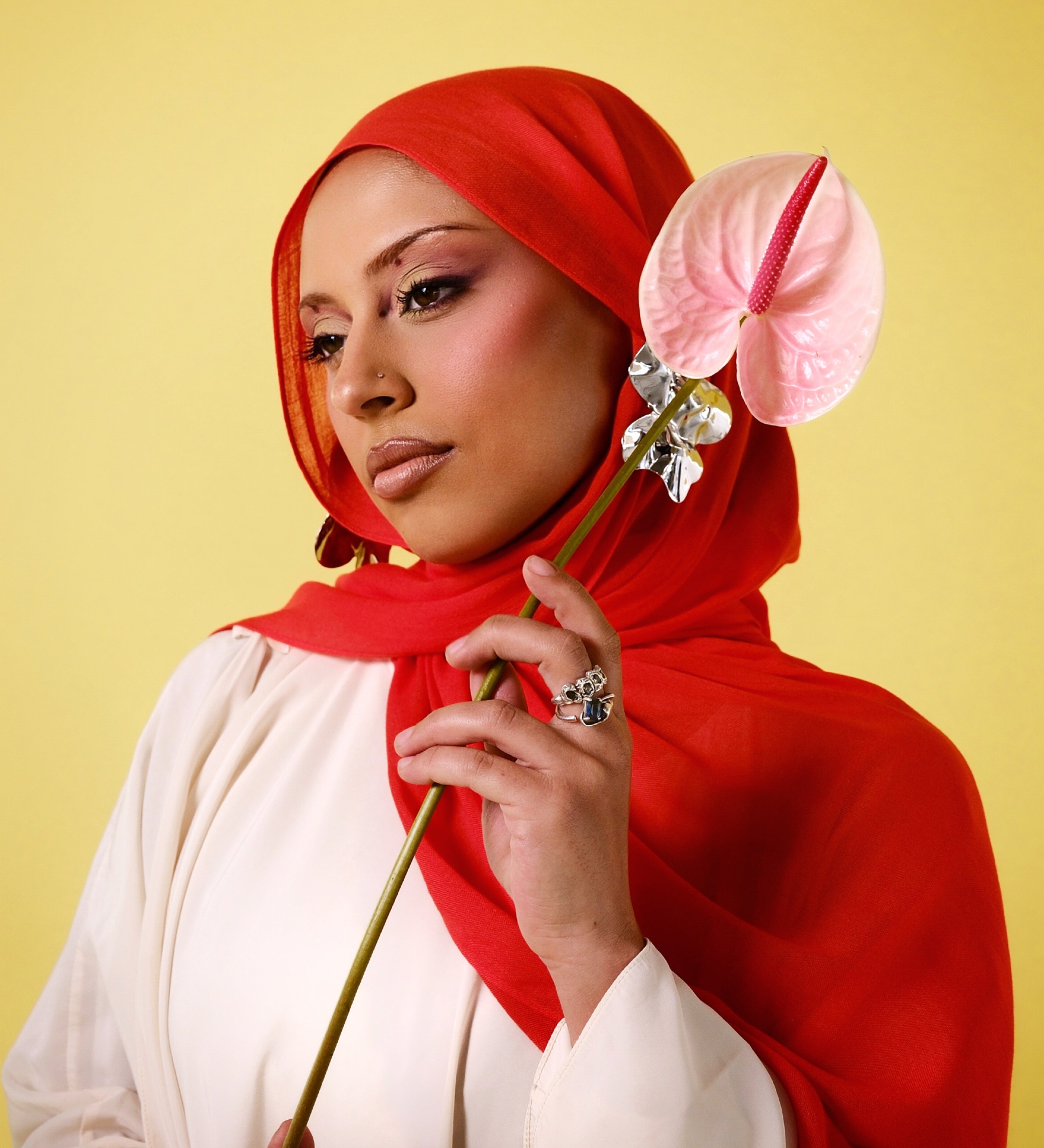 Woman wearing a red hijab holding a pink flower against a yellow background