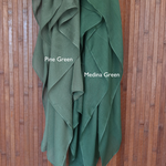 Color comparison of two green hijabs labeled 'Pine Green' and 'Medina Green' on a wooden background.