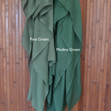Color comparison of two green hijabs labeled 'Pine Green' and 'Medina Green' on a wooden background.