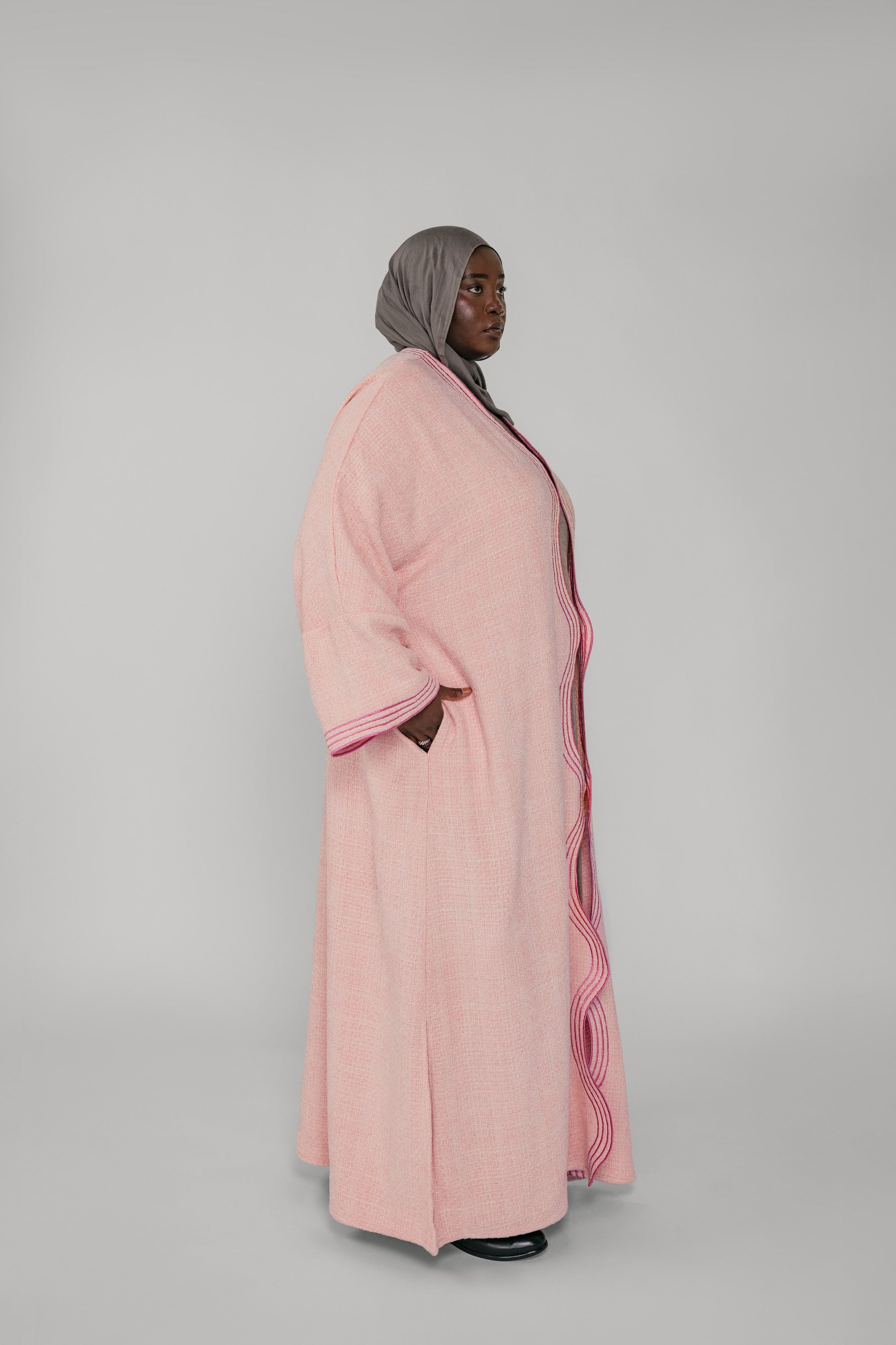 Woman wearing a pink abaya with a gray hijab on a white background