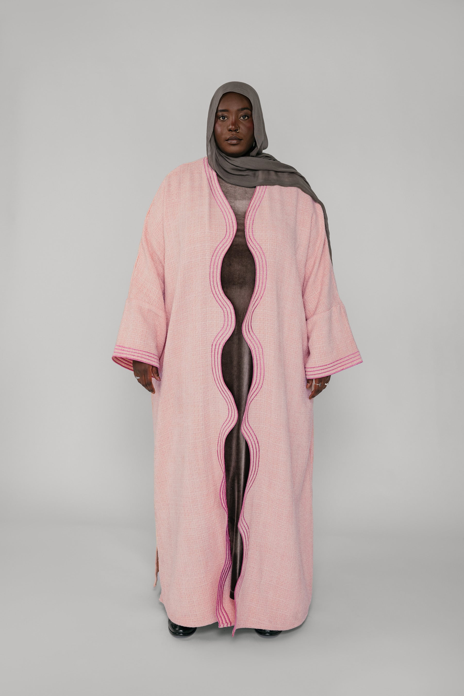 Person wearing a pink abaya with a gray hijab on a white background