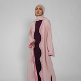 Woman wearing a pink abaya with a black dress underneath on a white background