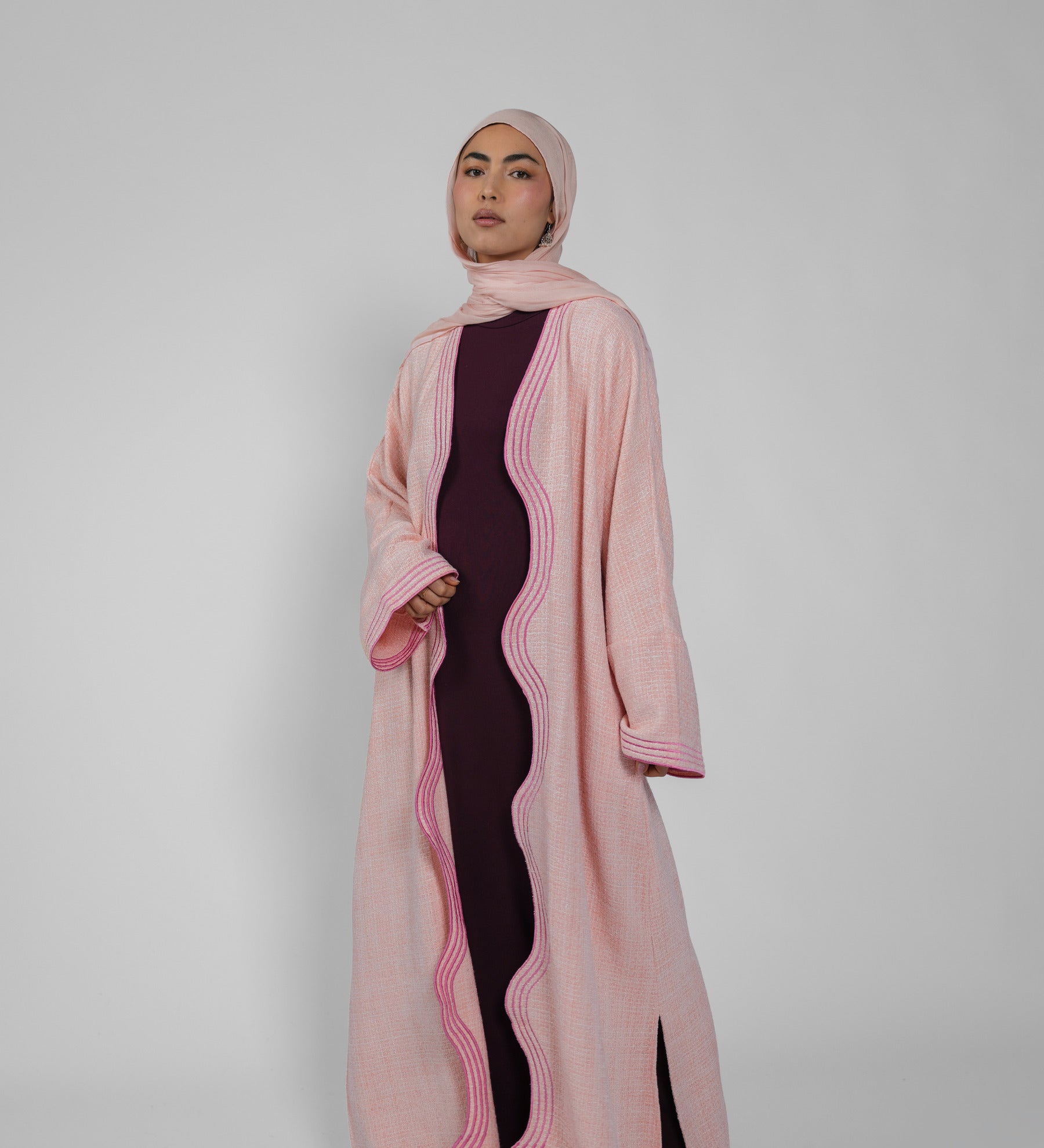 Woman wearing a pink abaya with a black dress underneath on a white background