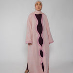 Woman wearing a pink abaya with a black dress underneath on a white background