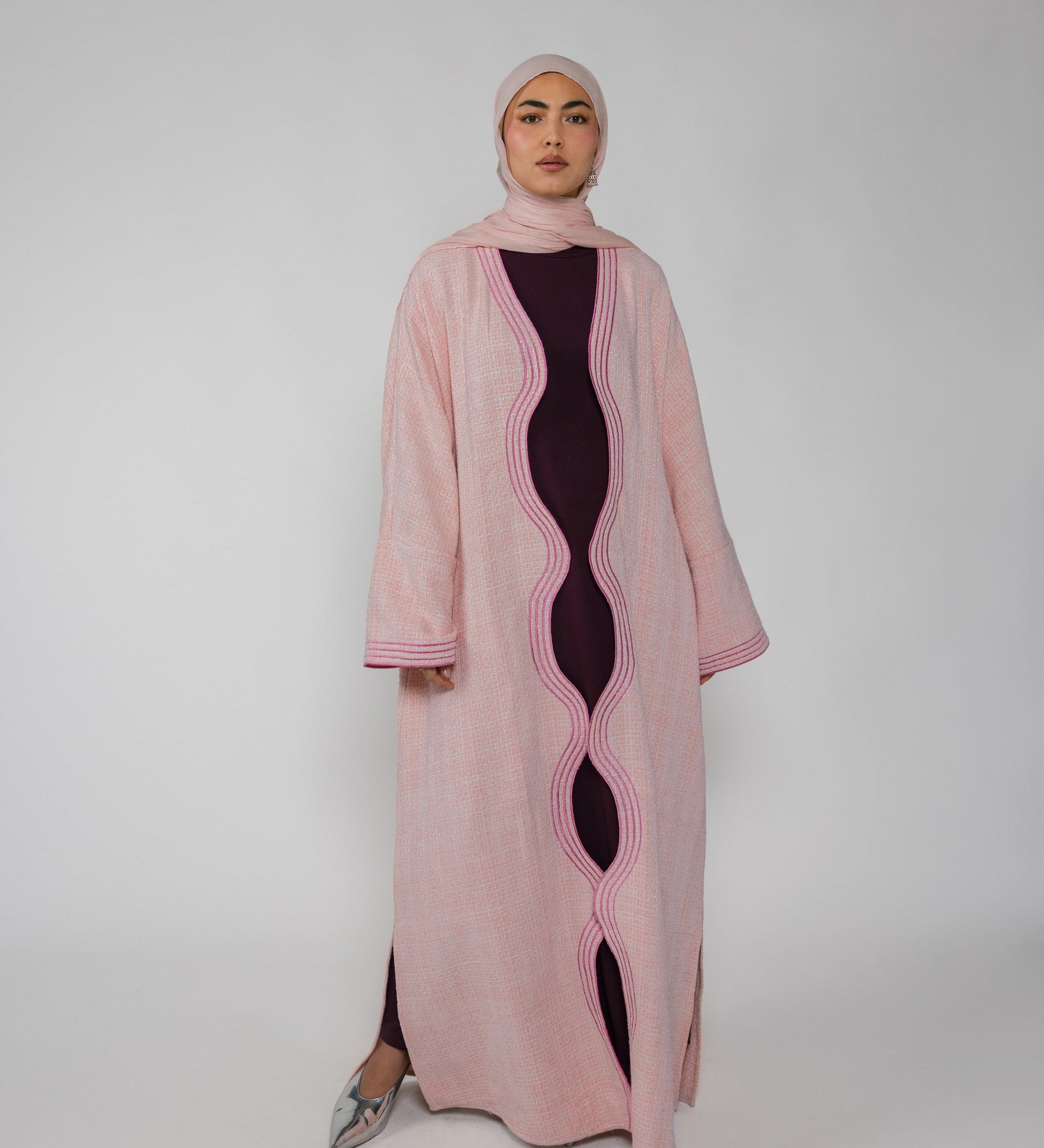 Woman wearing a pink abaya with a black dress underneath on a white background