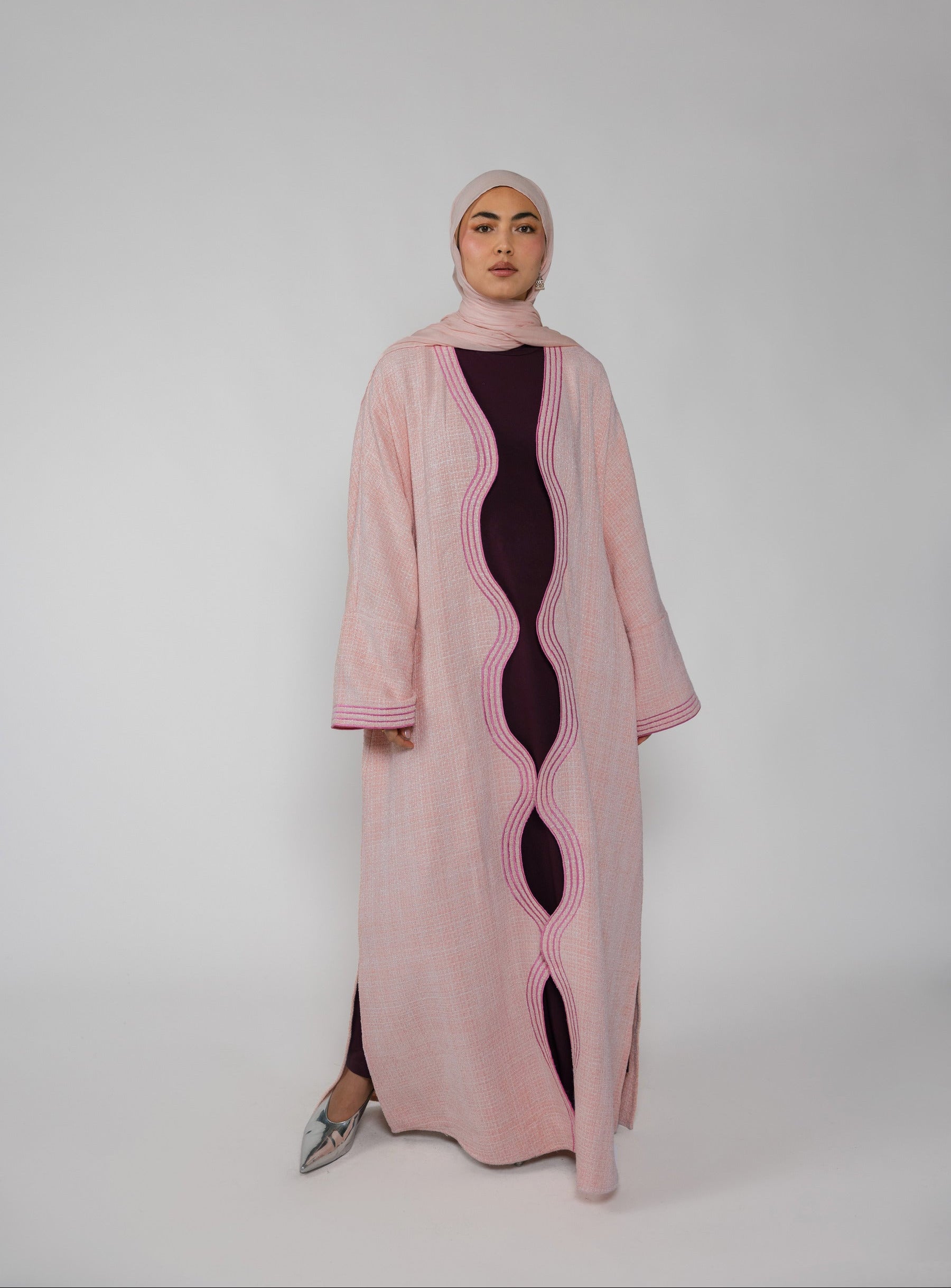 Woman wearing a pink abaya with a black dress underneath on a white background