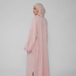 Person wearing a pink abaya and hijab on a light gray background