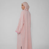 Person wearing a pink abaya and hijab on a light gray background