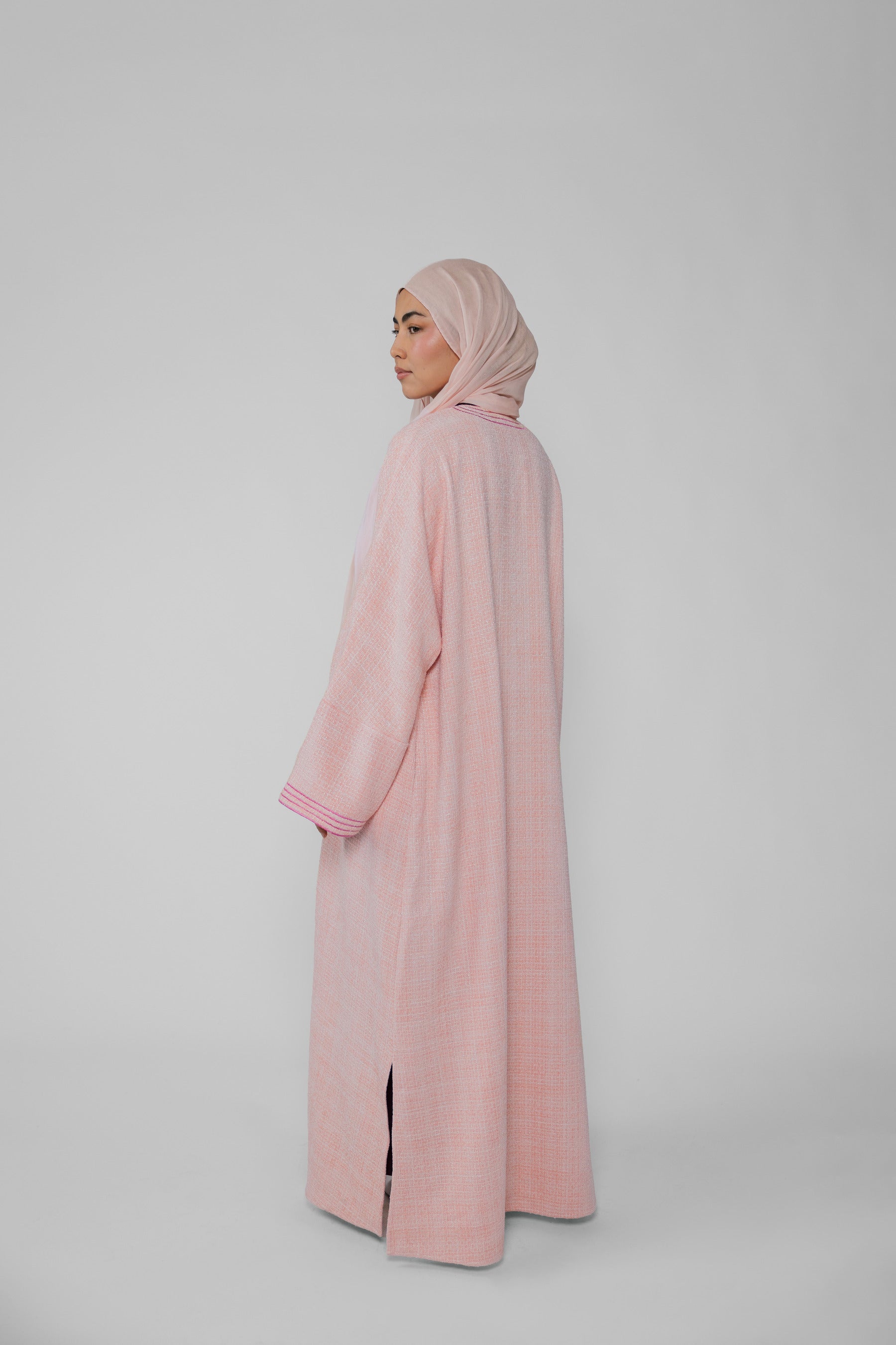 Person wearing a pink abaya and hijab on a light gray background