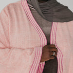 Person wearing a pink textured cardigan with a gray hijab and ring.