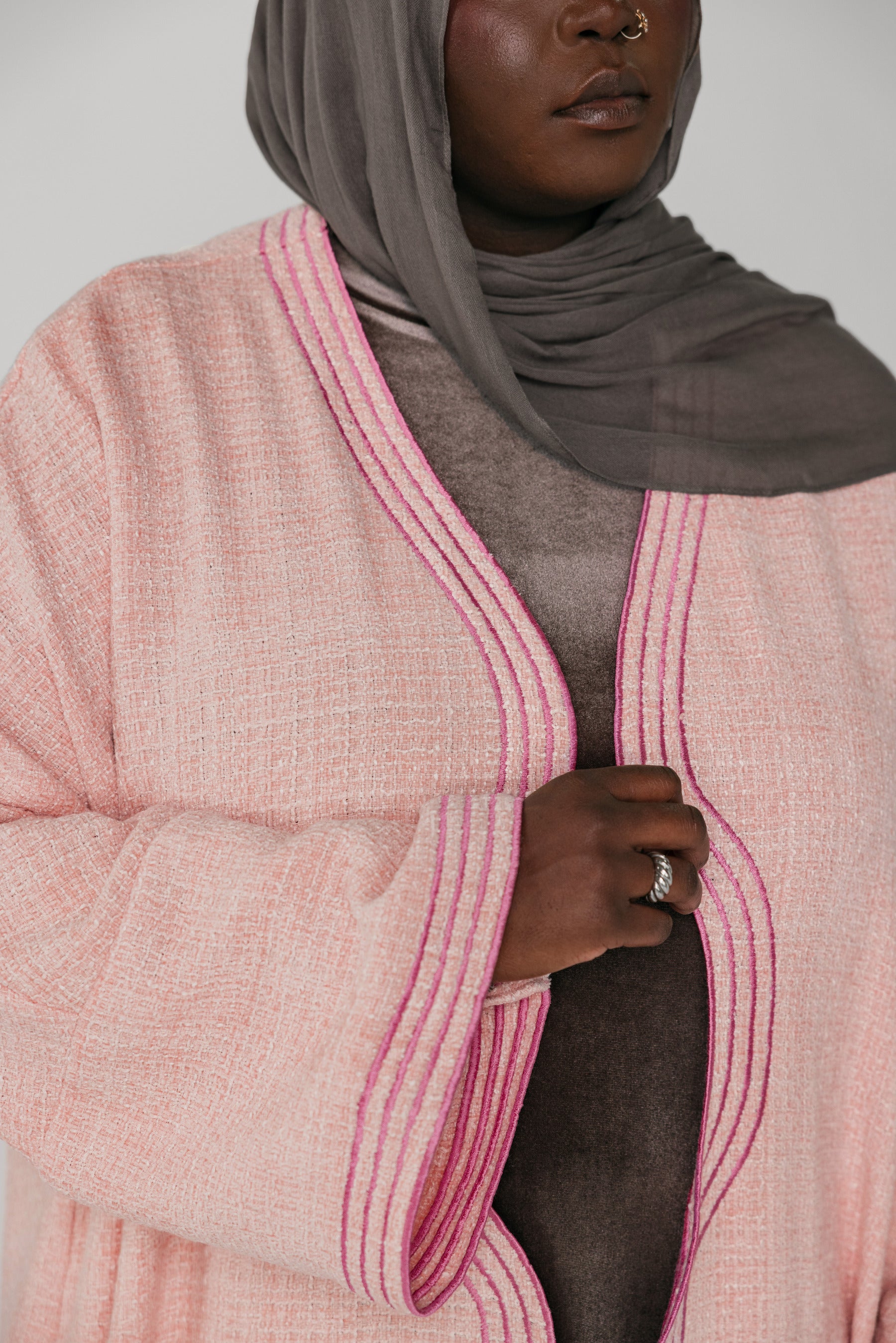 Person wearing a pink textured cardigan with a gray hijab and ring.