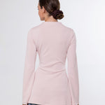A woman viewed from the back wearing a light pink long-sleeve top and blue jeans against a plain white studio background.