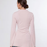 A woman viewed from the back wearing a light pink long-sleeve top and blue jeans against a plain white studio background.
