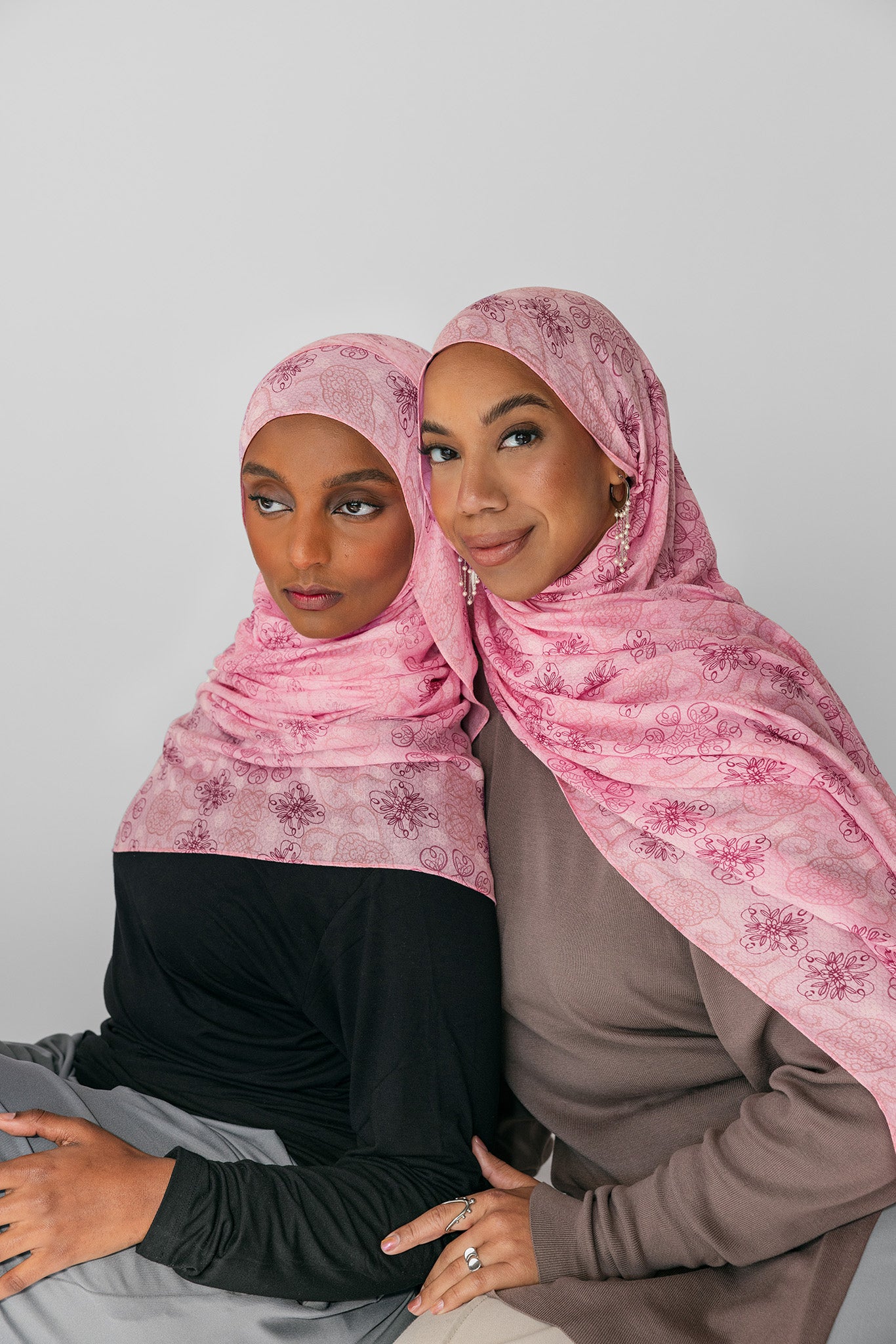 Two women wearing pink floral hijabs against a plain background