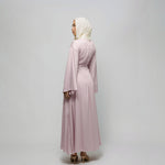 Woman wearing a light pink dress and hijab on a plain background