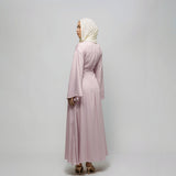 Woman wearing a light pink dress and hijab on a plain background