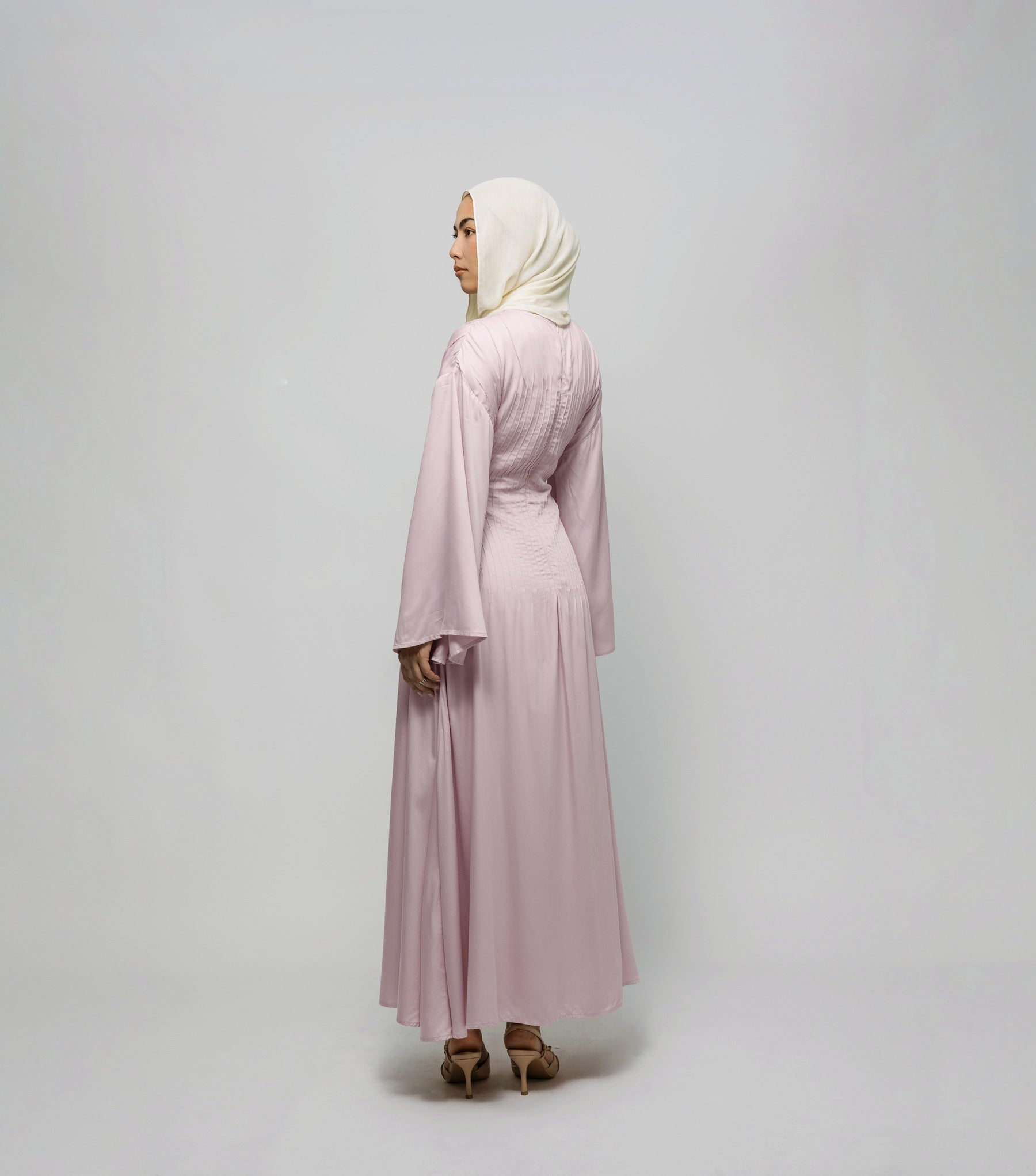 Woman wearing a light pink dress and hijab on a plain background