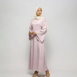 Woman wearing a light pink dress and hijab on a white background